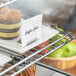 A stainless steel deli tag holder on a metal shelf holding deli tags.