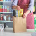 A hand putting a bag of food into a Choice natural kraft paper bag.