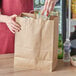 A person holding a Choice Natural Kraft paper bag filled with food.