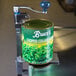 An Edlund Standard Duty Can Opener clamped to a metal stand opening a can of chopped collard greens.