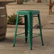 A Lancaster Table & Seating emerald green metal outdoor counter height stool on a stone patio.