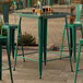 A Lancaster Table & Seating emerald green bar table on a stone surface.