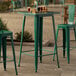 A Lancaster Table & Seating emerald green bar table on a stone patio.