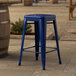 A blue Lancaster Table & Seating outdoor backless counter height stool sitting on a stone surface.