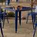 A Lancaster Table & Seating blue metal table with chairs on a patio.