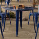 A Lancaster Table & Seating blue metal outdoor table with blue chair legs.