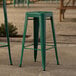 Two green Lancaster Table & Seating outdoor barstools on a stone patio.