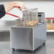 A person using a Cecilware countertop deep fryer to fry a basket of food.