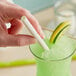 A person holding a Sorbos lime flavored paper straw in a glass of green liquid.