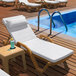 A Lancaster Table & Seating Sand resin chaise with white cushion and pillow next to a pool.