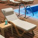A Lancaster Table & Seating resin chaise with cream cushions and a pillow next to a pool.