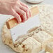 A person using a Fox Run stainless steel dough cutter with a wood handle to cut dough.