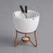 A white ceramic fondue pot with metal handles and two forks.