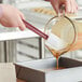 A person pouring liquid into a pan with a Choice heat-resistant silicone spatula.