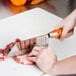 A person using a Thunder Group stainless steel cleaver to cut meat on a cutting board.