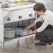 A person in an apron putting utensils in a ServIt steam table container.