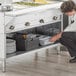 A woman kneeling down in front of a ServIt electric steam table on a counter in a school kitchen.