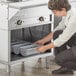 A woman using a fork to put food in a pan in a professional kitchen.