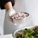 A person in gloves holding a Vollrath stainless steel mixing bowl filled with chopped onions.