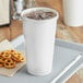 A white Choice paper cold cup with a lid and straw filled with ice on a tray with pretzels.