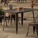 A Lancaster Table & Seating copper outdoor table on a stone patio with a chair underneath.