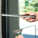 A person using an Unger 12" metal rod to clean a window.