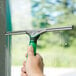 A hand holding a Unger green and black squeegee to a window.