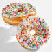 A pair of donuts with white icing and colorful rainbow sprinkles.