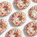 A group of donuts with white icing and colorful rainbow sprinkles.