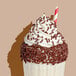 A milkshake topped with whipped cream and chocolate sprinkles, served with a red and white striped straw.