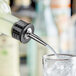 A bartender using a stainless steel liquor pourer to pour a drink into a glass.
