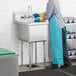 A person wearing blue apron and gloves washing dishes in a Regency stainless steel commercial sink.