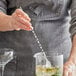 An American Metalcraft stainless steel twisted bar spoon being used to mix a drink in a glass.