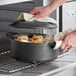 A hand using a white towel to clean a Valor pre-seasoned cast iron dutch oven.