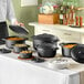 A woman pouring food into a black Valor cast iron Dutch oven.