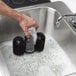 A person using a Bar Maid manual glass washer to clean a glass in a sink.