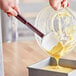 a spoon pouring yellow liquid into a metal container