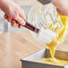 A Mercer Culinary Hell's Tools silicone spatula mixing yellow liquid in a bowl.