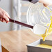 A person using a Mercer Culinary Hell's Tools spoonula to pour yellow liquid into a pan.