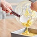 A hand using a Mercer Culinary Hell's Tools spoonula to pour yellow batter into a pan.