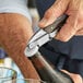 A person using an Acopa Flex Waiter's Corkscrew with a dark wood handle to open a bottle of beer on a counter.