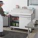 An Avantco stainless steel sandwich prep table on a counter with food containers and a bowl of green leaves.