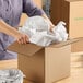 A person placing crumpled newsprint packing paper into a cardboard box.