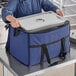 A woman in a blue uniform holding a large blue Choice insulated cooler bag with a metal tray inside.