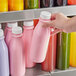 A hand holding a 16 oz. round clear PET juice bottle full of pink liquid.