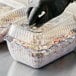 A person in black gloves using a clear plastic Choice deli container to serve food.