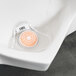 A white plastic mesh Lavex urinal screen with a round orange citrus block in it.