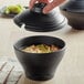 A person holding a lid over a Nara black melamine bowl of soup.