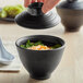 A person holding a black GET Nara bowl lid over a bowl of food.