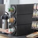 A woman using a Choice Black Stackable Countertop Cup Dispenser to fill a cup with coffee.